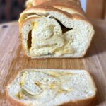 a loaf of homemade garlic cheese bread with the end sliced off showing the cheese rolled into the center of the loaf